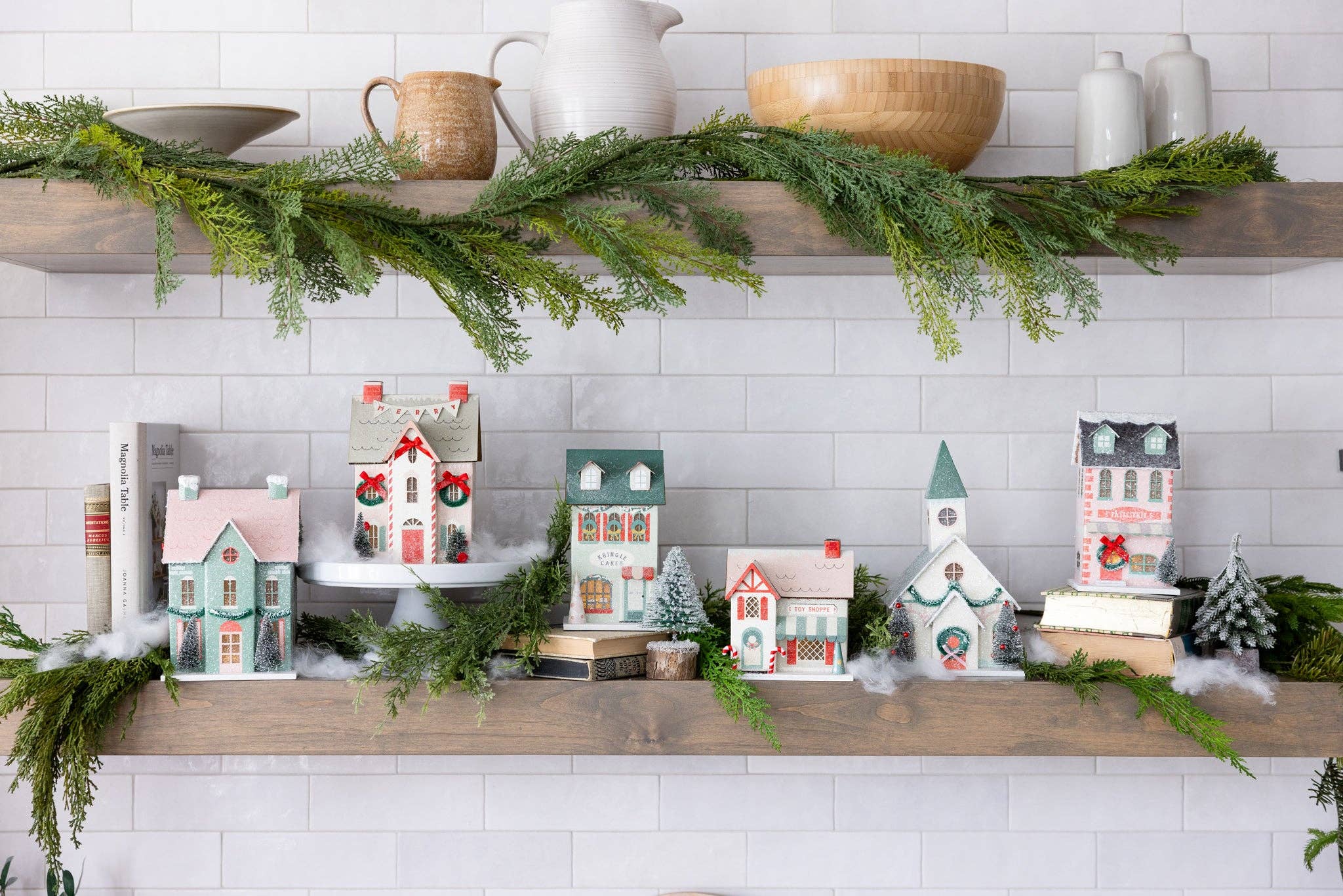 Decorative shelves with Christmas-themed village houses and greenery on a white tiled wall.