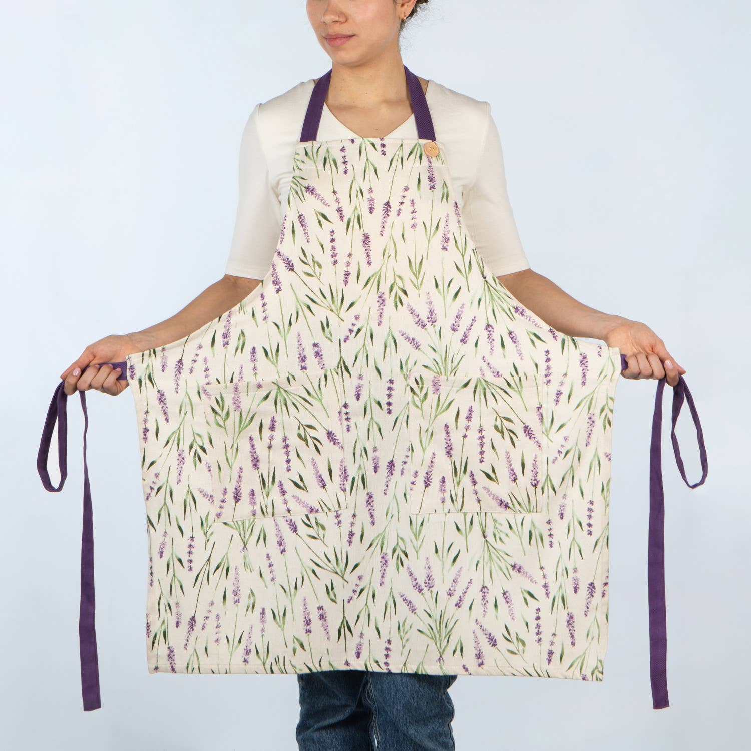 Person holding a floral apron with lavender design on a plain background