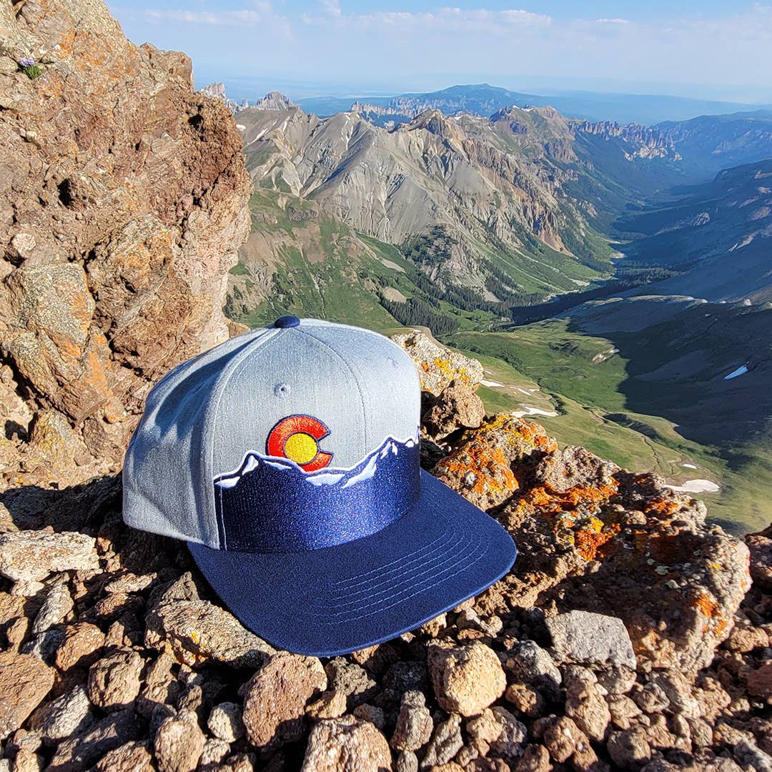 Cap with a logo on a rocky mountain top with a scenic view of mountains and valleys.