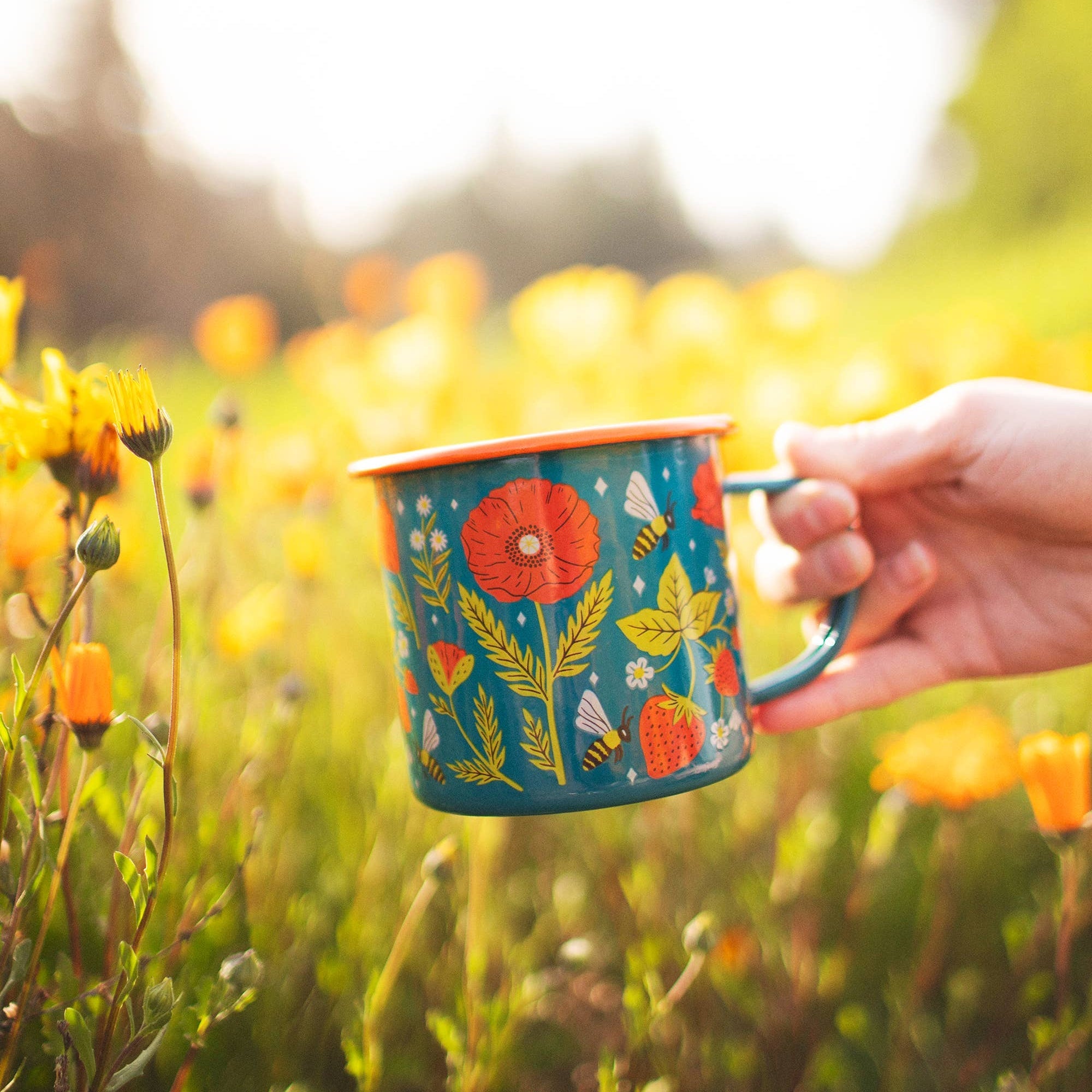 Hand holding a colorful mug with floral design in a field of yellow flowers
