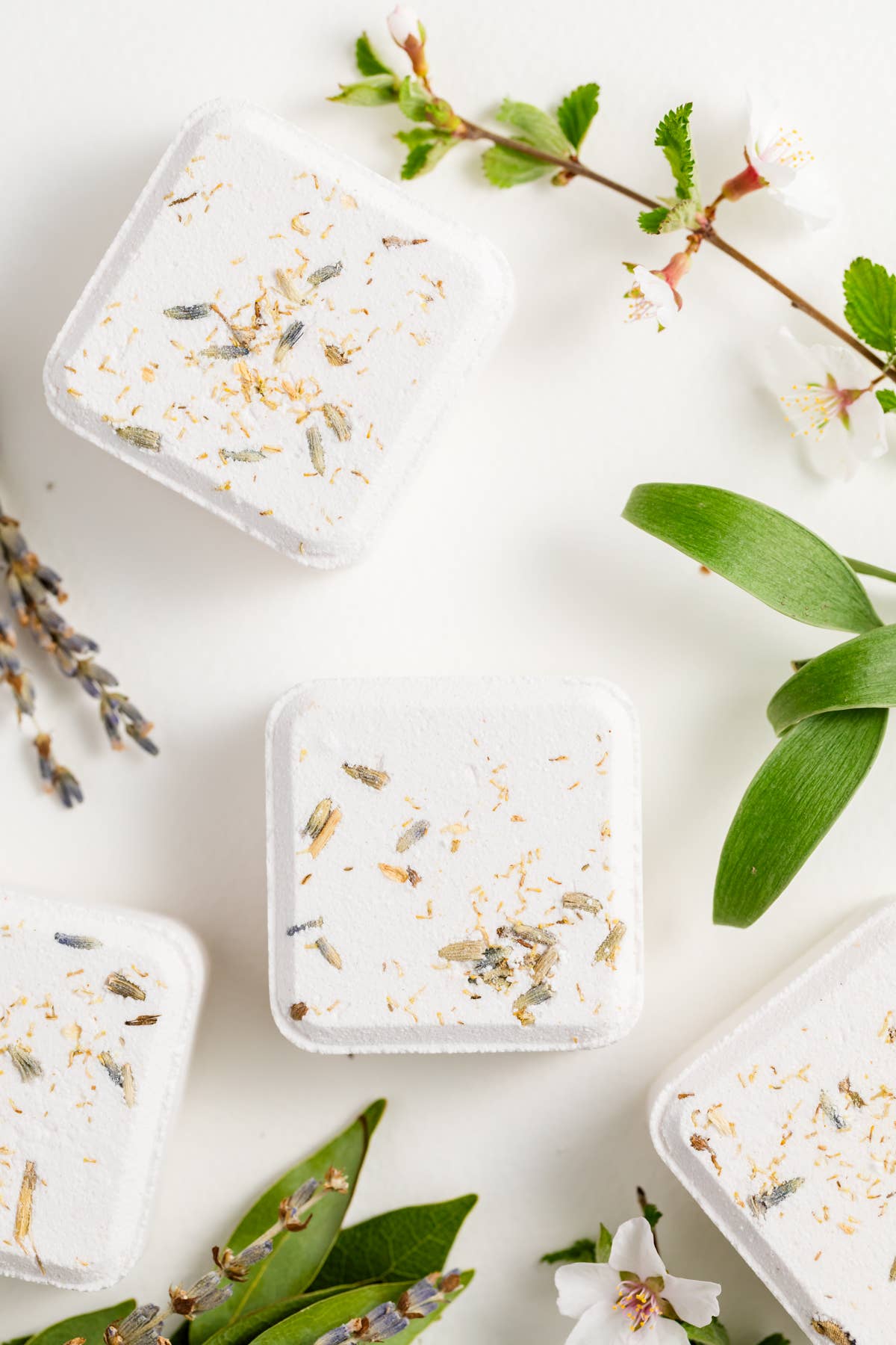 White shower steamers with natural elements on a light background with green leaves and flowers.