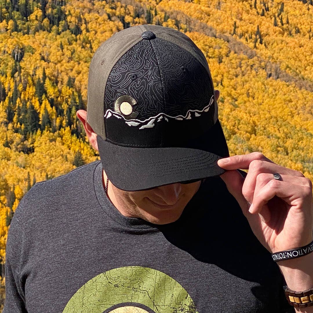 Person wearing a cap with a mountain design against a backdrop of yellow trees