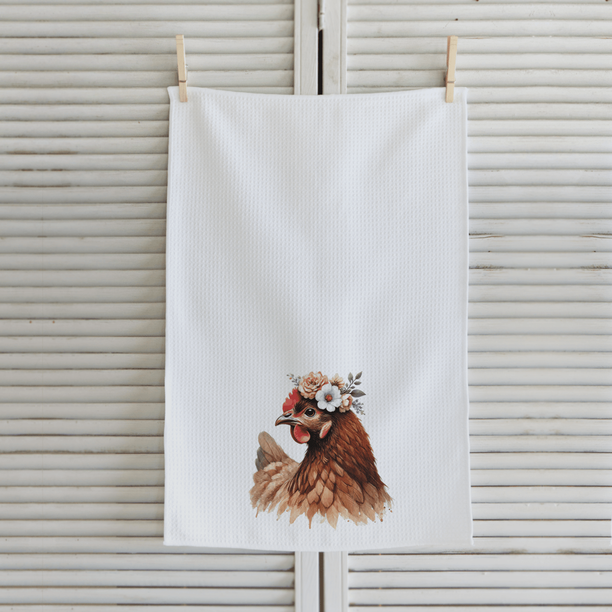 White towel with a chicken illustration wearing a flower crown hanging on a wooden surface.