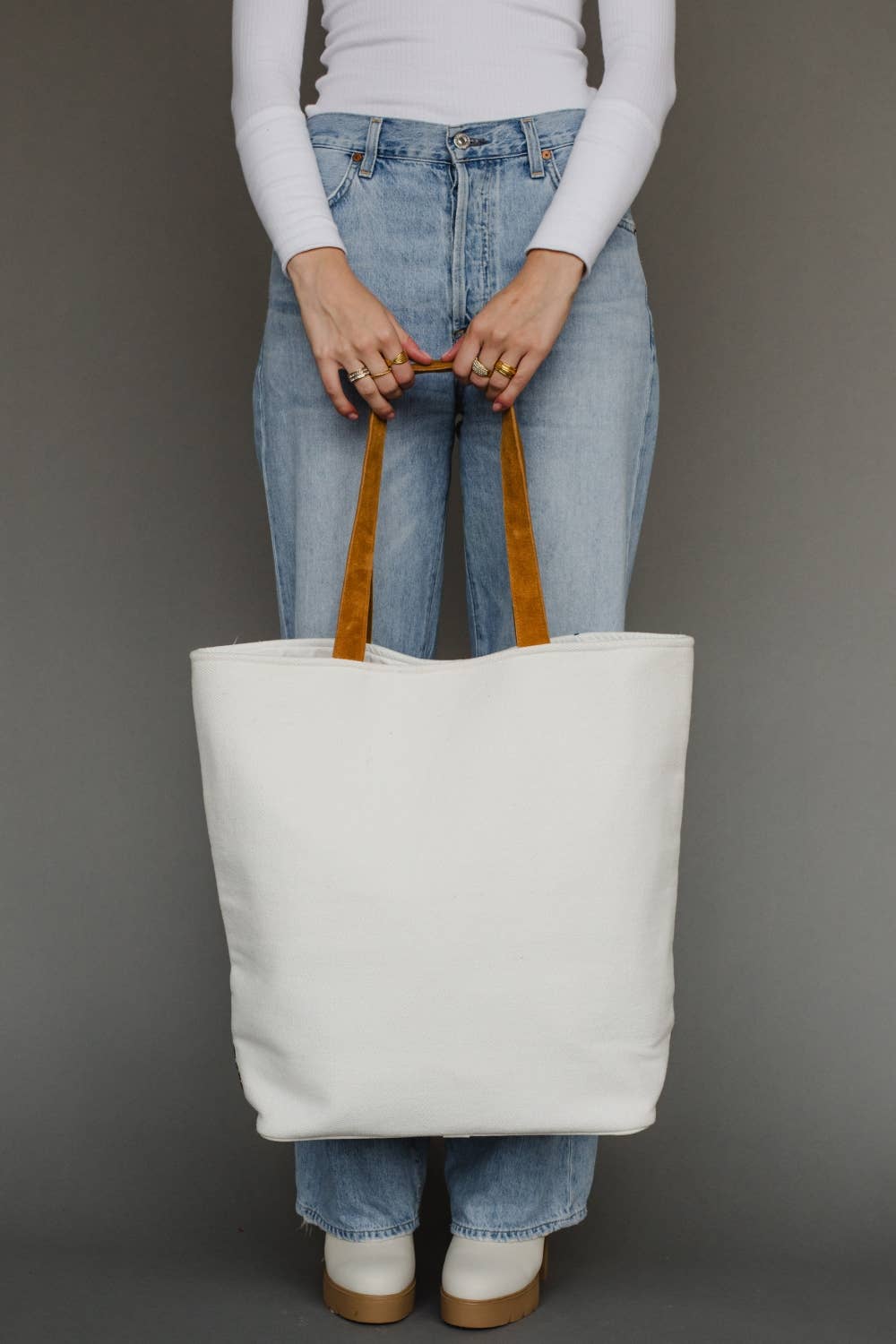 Person holding a white tote bag with brown handles against a gray background