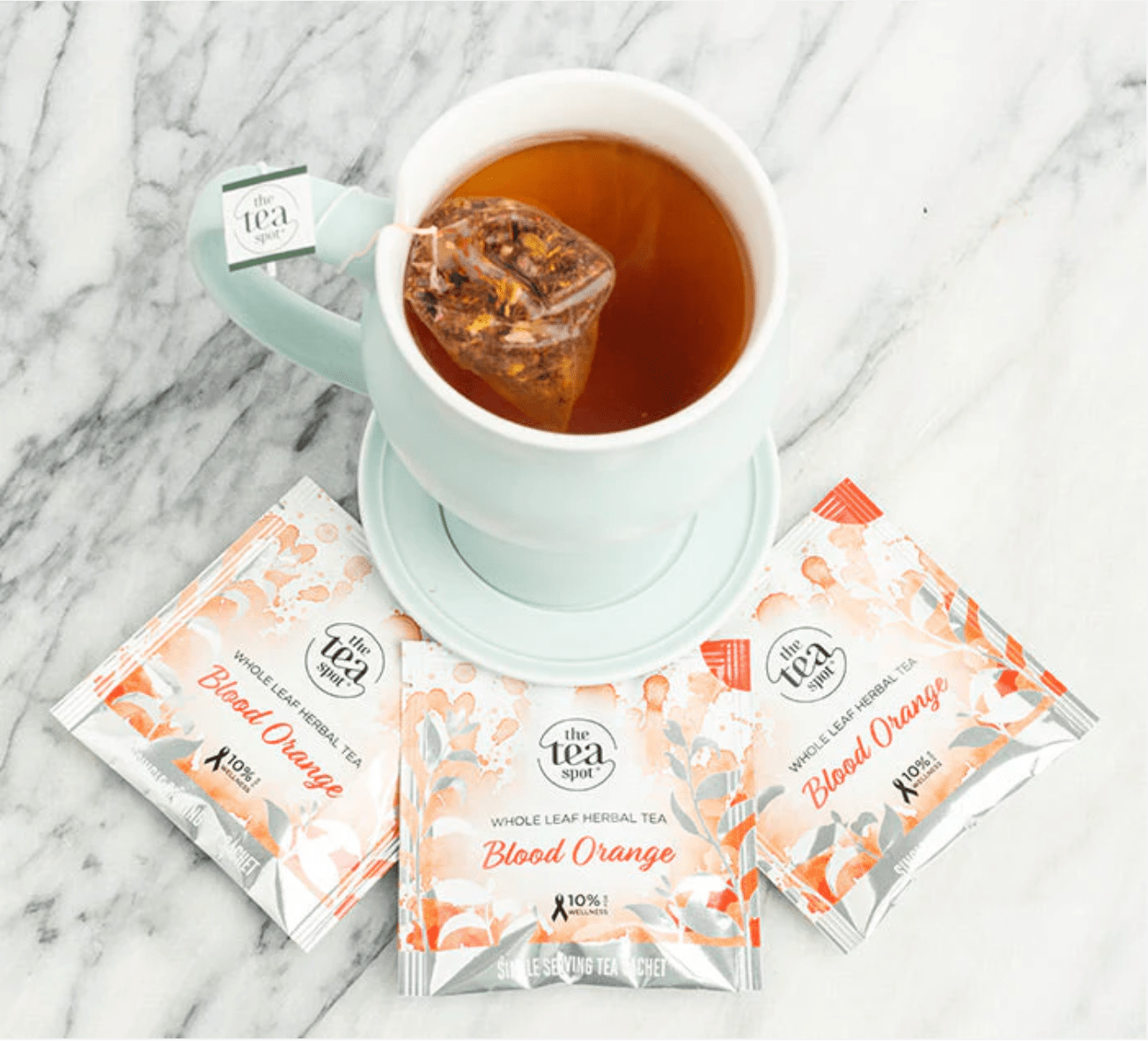 Tea cup with a blood orange tea bag and three packets of the same tea on a marble surface.