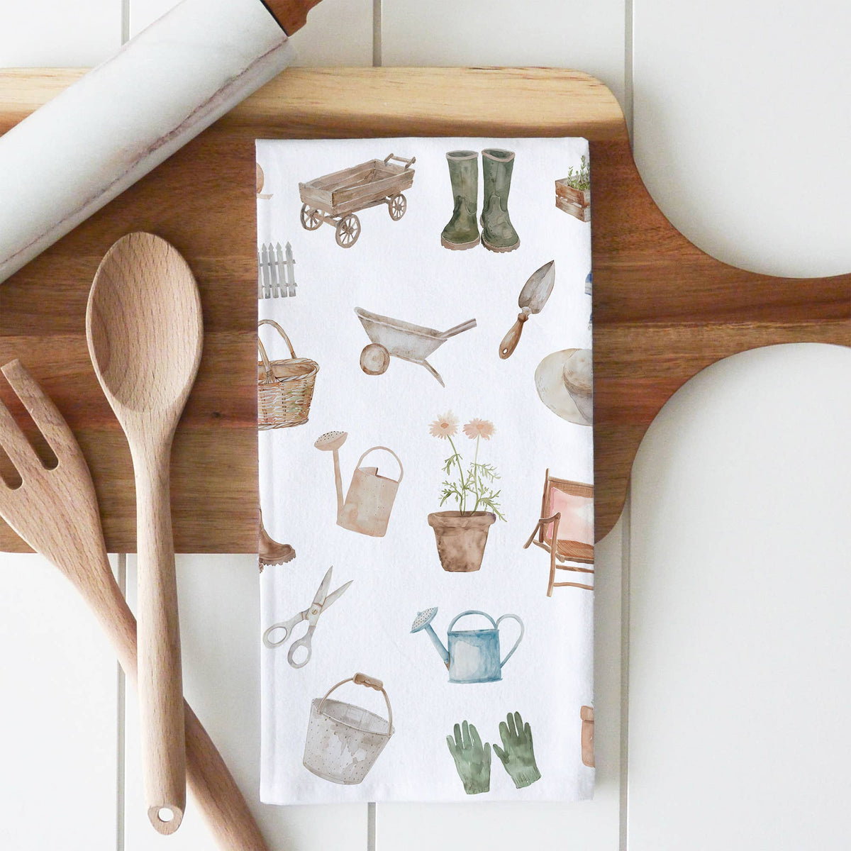 Gardening-themed towel with tools and plants on a wooden cutting board with utensils.