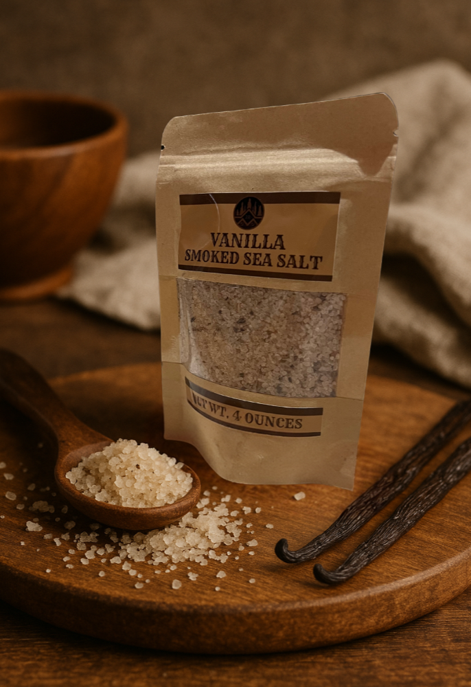 Packaged vanilla smoked sea salt on a wooden surface with a spoonful of salt and vanilla beans.