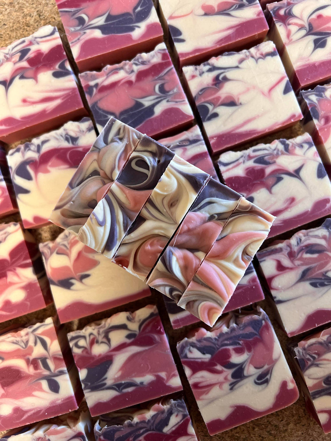 Marbled soap bars with pink, purple, and beige colors arranged on a wooden surface.