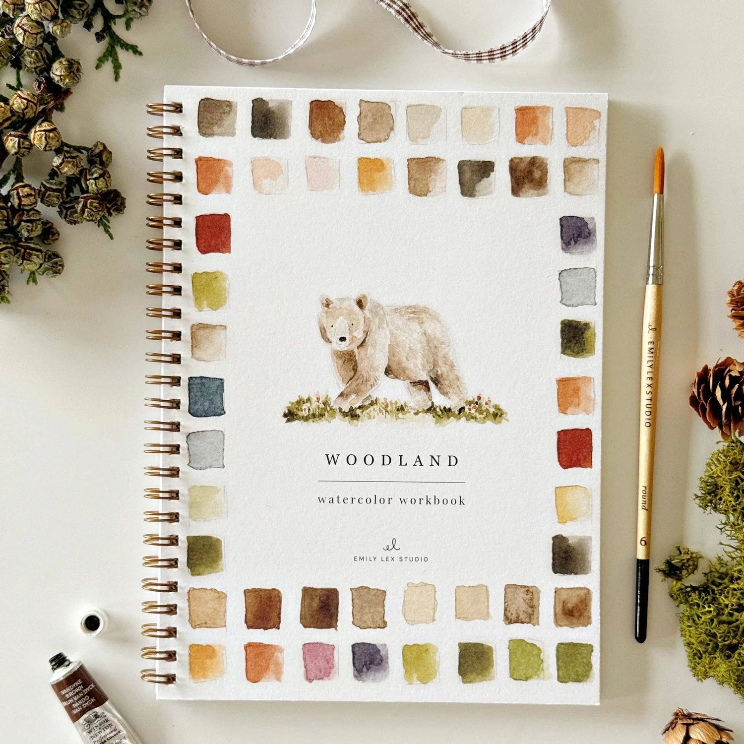 Woodland watercolor workbook with a bear illustration on a white surface with decorative elements.