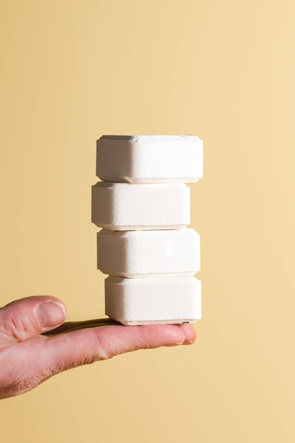 Hand holding a stack of white shower steamer blocks against a beige background