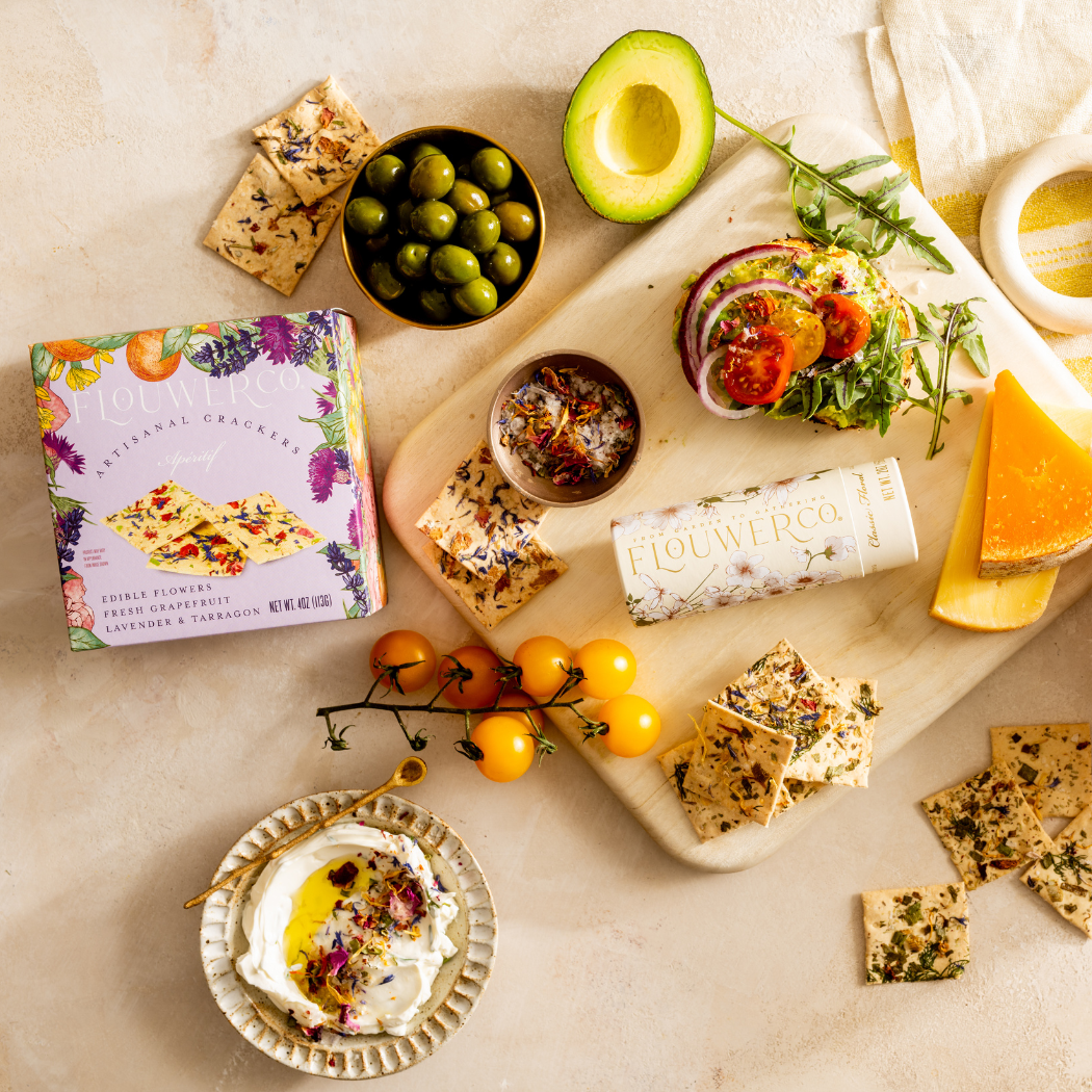 Assorted snacks and appetizers on a wooden board with a box of crackers.