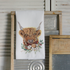 Tea towel with a highland cow design on a wooden surface