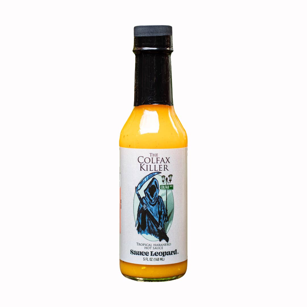 A bottle of The Colfax Killer Tropical Habanero Sauce with a label featuring a stylized, monochrome illustration of a figure standing in the shadows, surrounded by a vibrant, orange-yellow background.