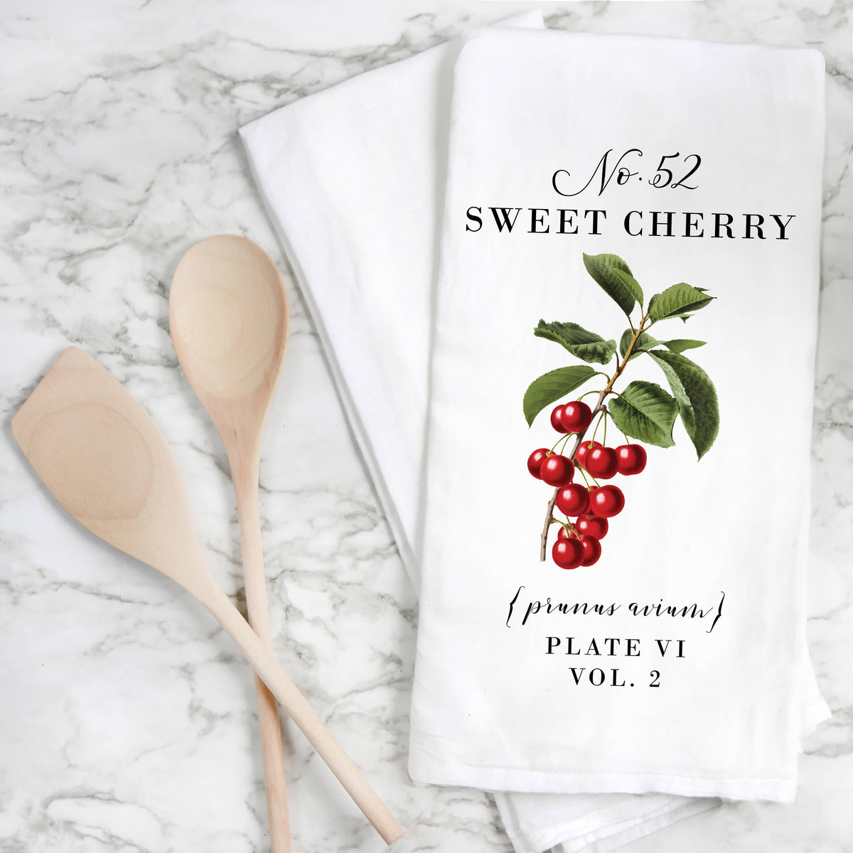 A white kitchen towel with a vintage-style illustration of red cherries and green leaves, printed with the text &