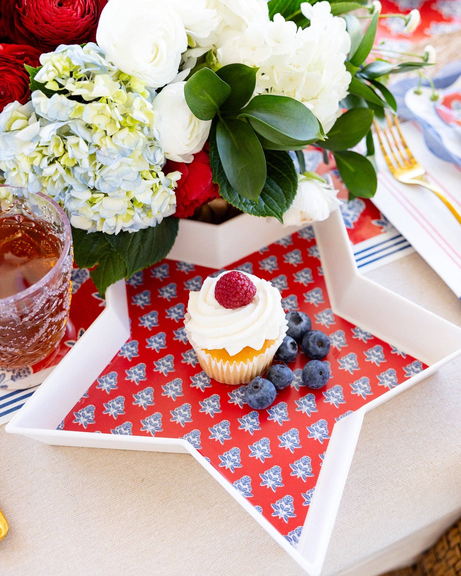Cupcake with berries on a decorative bamboo tray with flowers in the background
