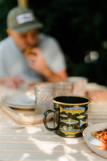 Person sitting at a table with a mug featuring fish designs, blurred background