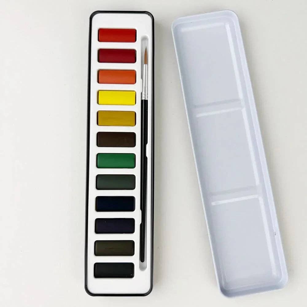 Set of watercolor paints with a brush in a transparent case on a light gray background