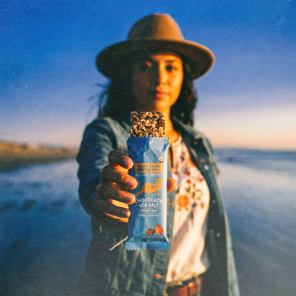 Person holding a chocolate sea salt snack bar against a scenic background