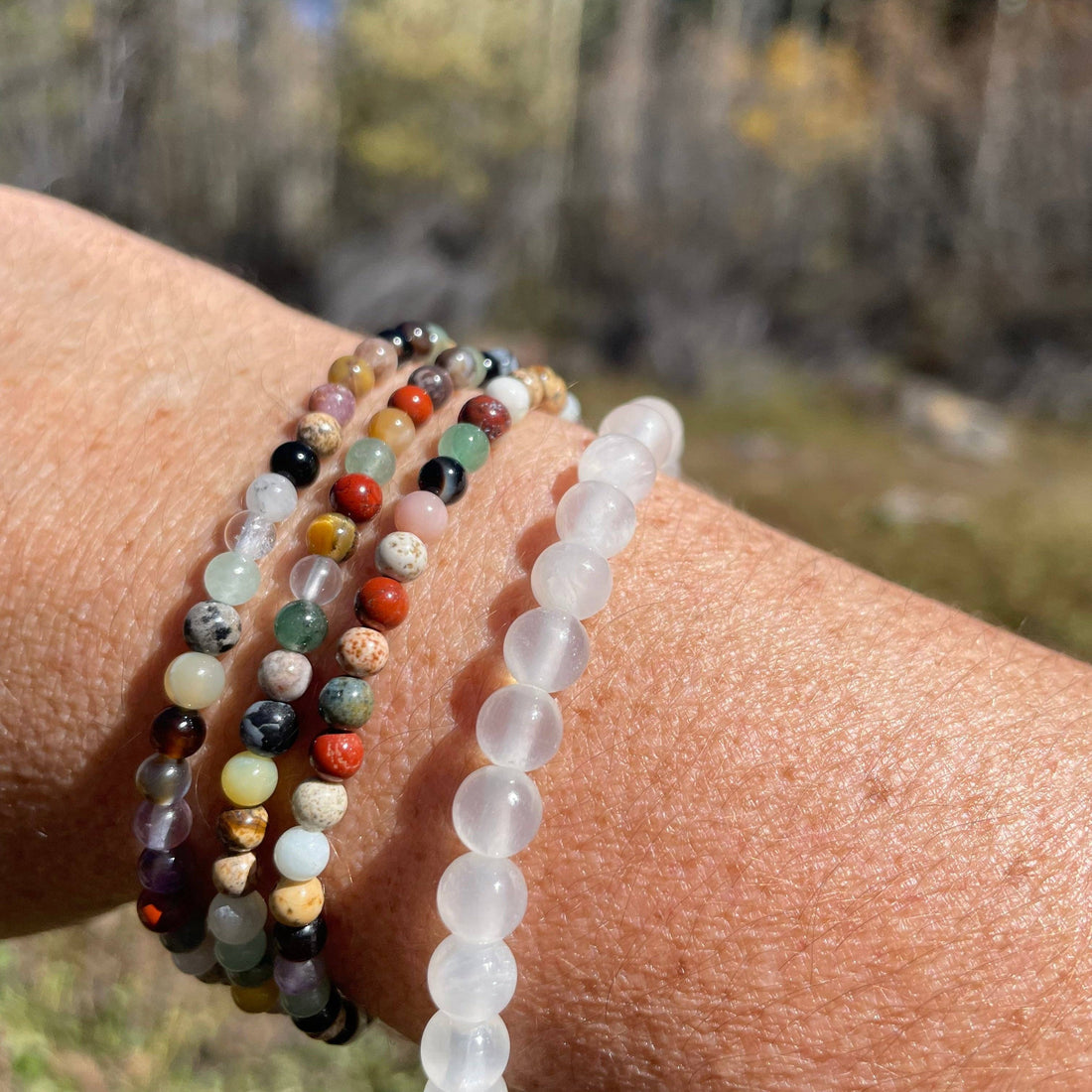 Close-up of a wrist wearing four beaded bracelets with a natural background