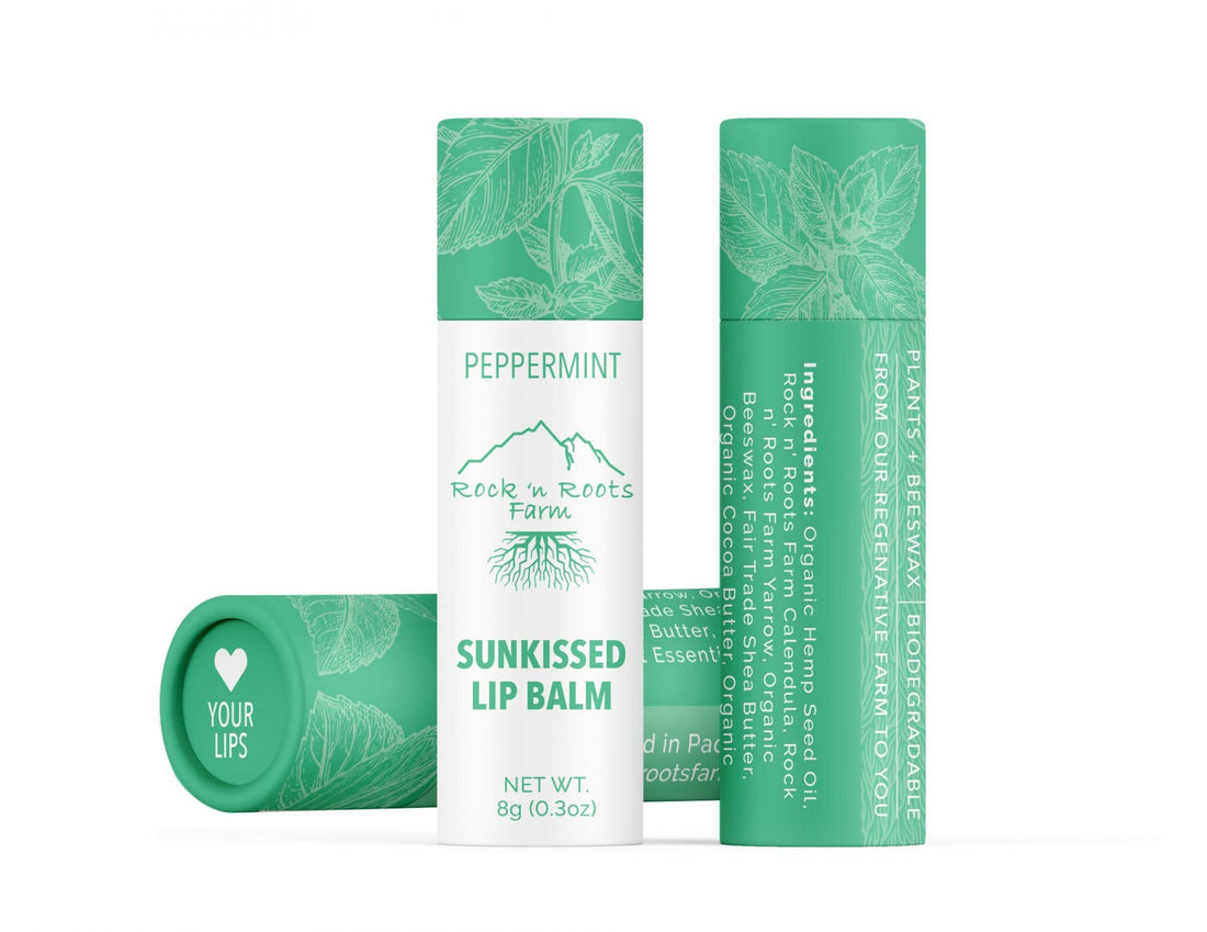 A tube of Sun Kissed Lip Balm with peppermint flavor, organic mandarin essential oil, and natural ingredients. The packaging is green with text and branding.
