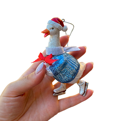 Decorative goose ornament wearing a Santa hat and blue dress held by a hand on a white background