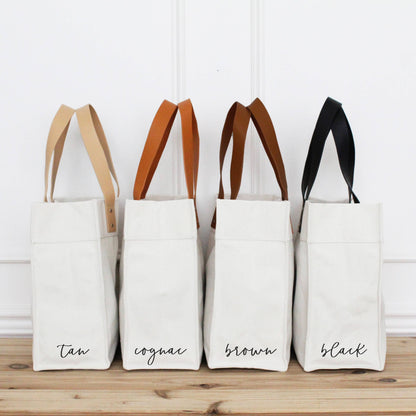 Four white tote bags with different colored handles on a wooden surface.