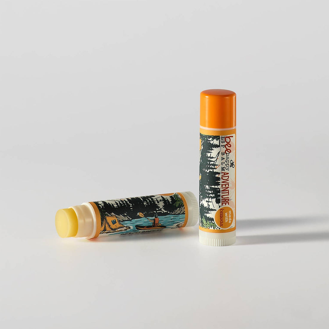Two lip balm tubes with forest design and orange caps on a light gray background