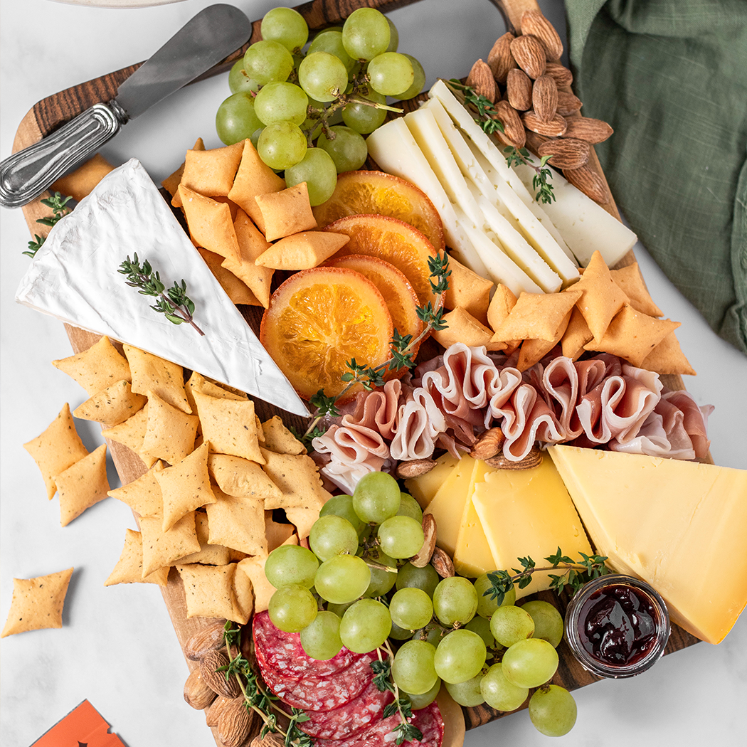 Assorted cheese, crackers, and fruits on a wooden board with a knife.