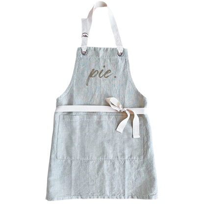 A light blue-gray linen apron with white straps and a white waist tie, featuring the word &