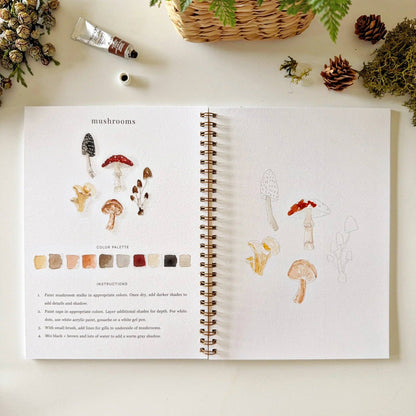 Open book with illustrations of mushrooms and color palette on a table with decorative items.