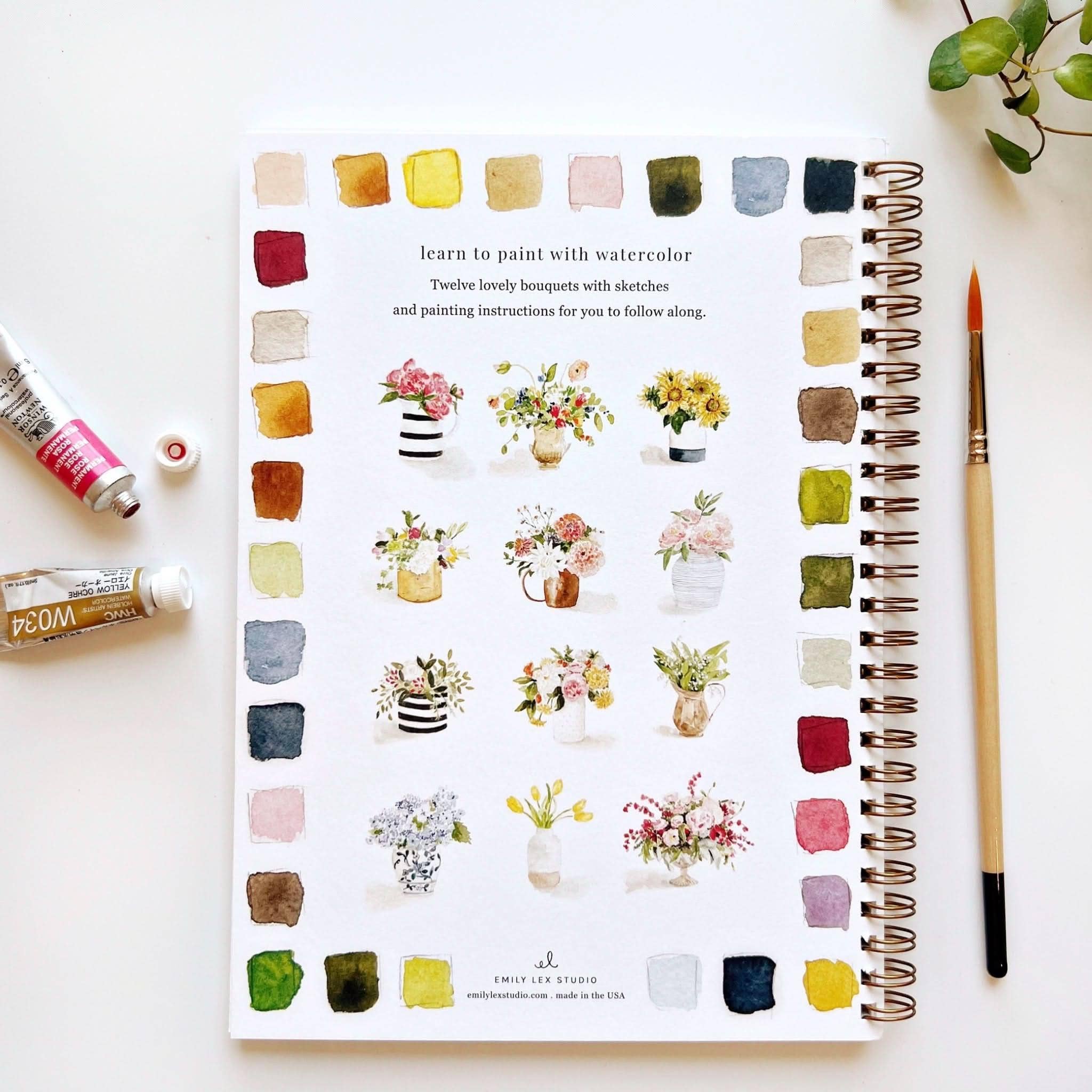 Notebook with watercolor flower designs and painting tools on a white surface