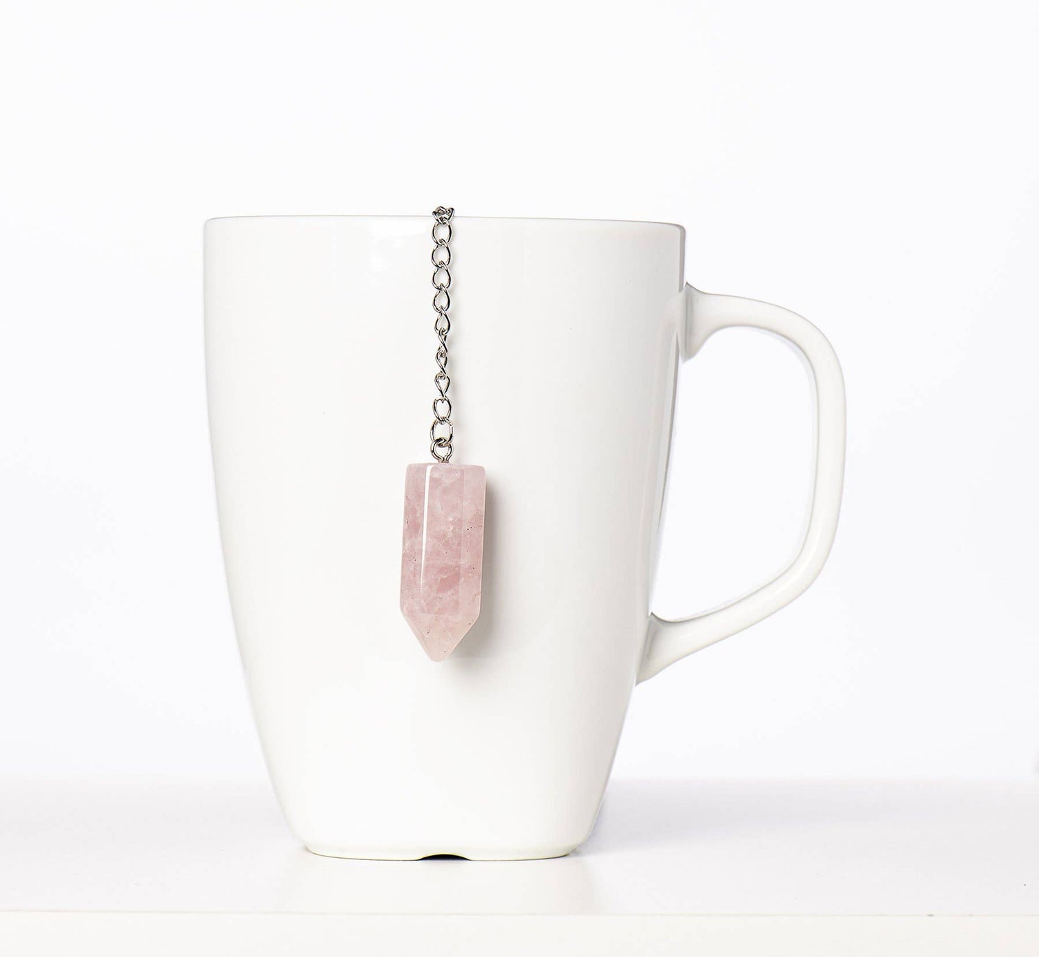 White mug with a pink stone tea bag infuser on a white background