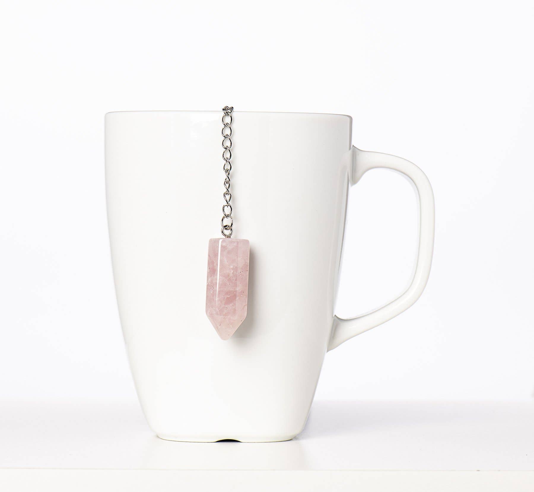 White mug with a pink stone tea bag infuser on a white background