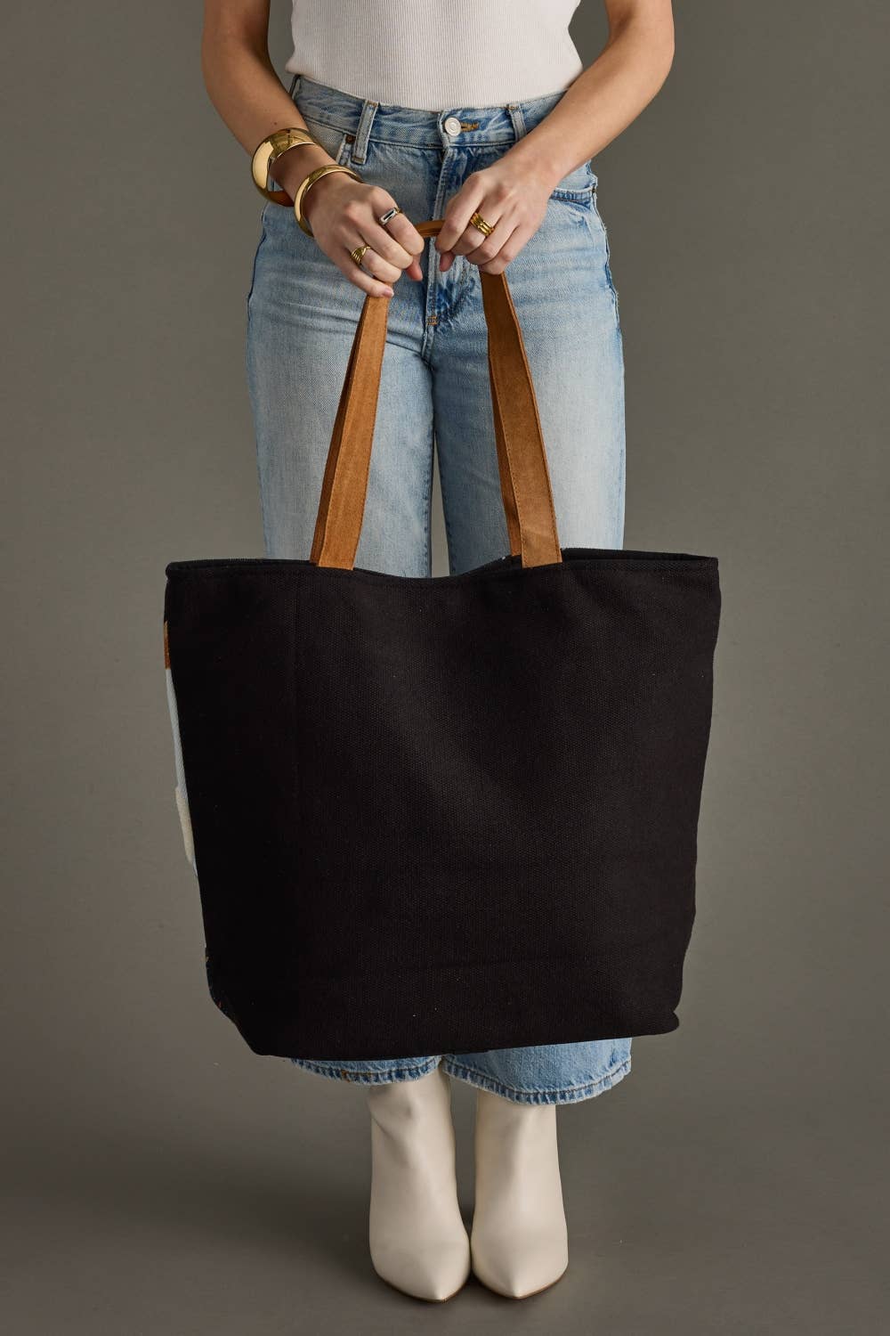 Person holding a black tote bag with brown handles against a gray background