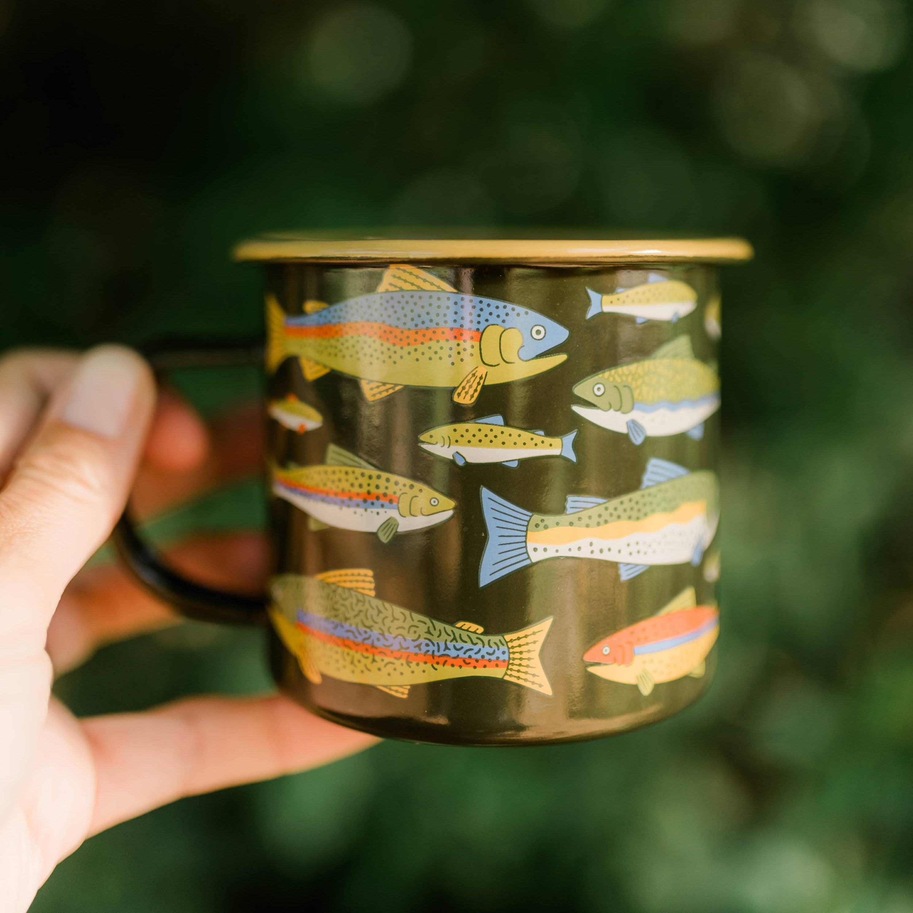 Hand holding a mug with fish illustrations against a blurred green background
