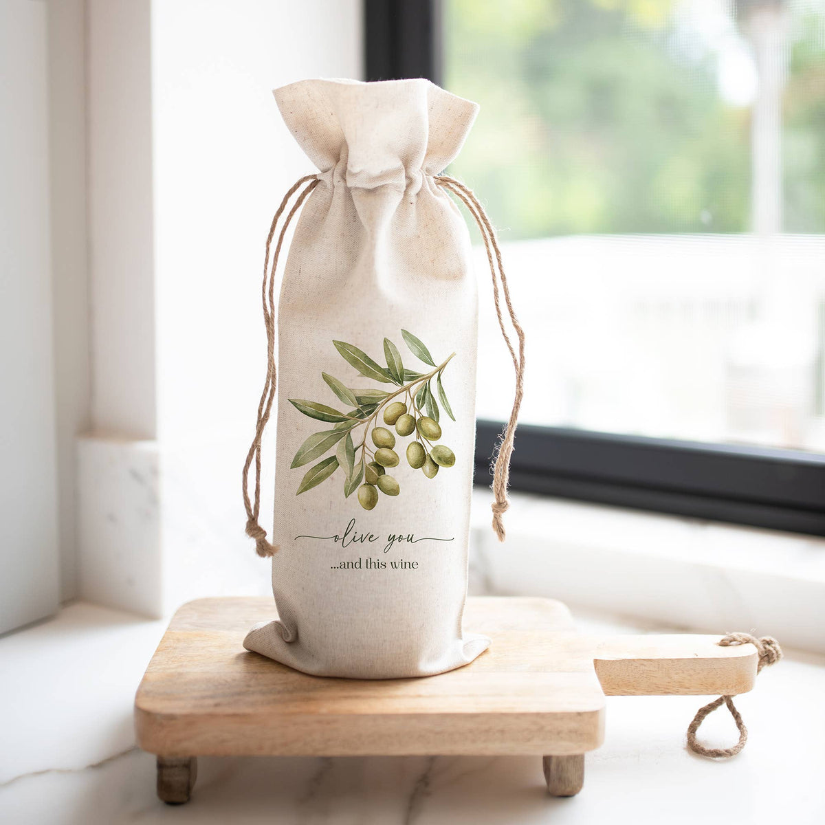 A beige drawstring wine bottle bag with a green olive branch illustration and the text &