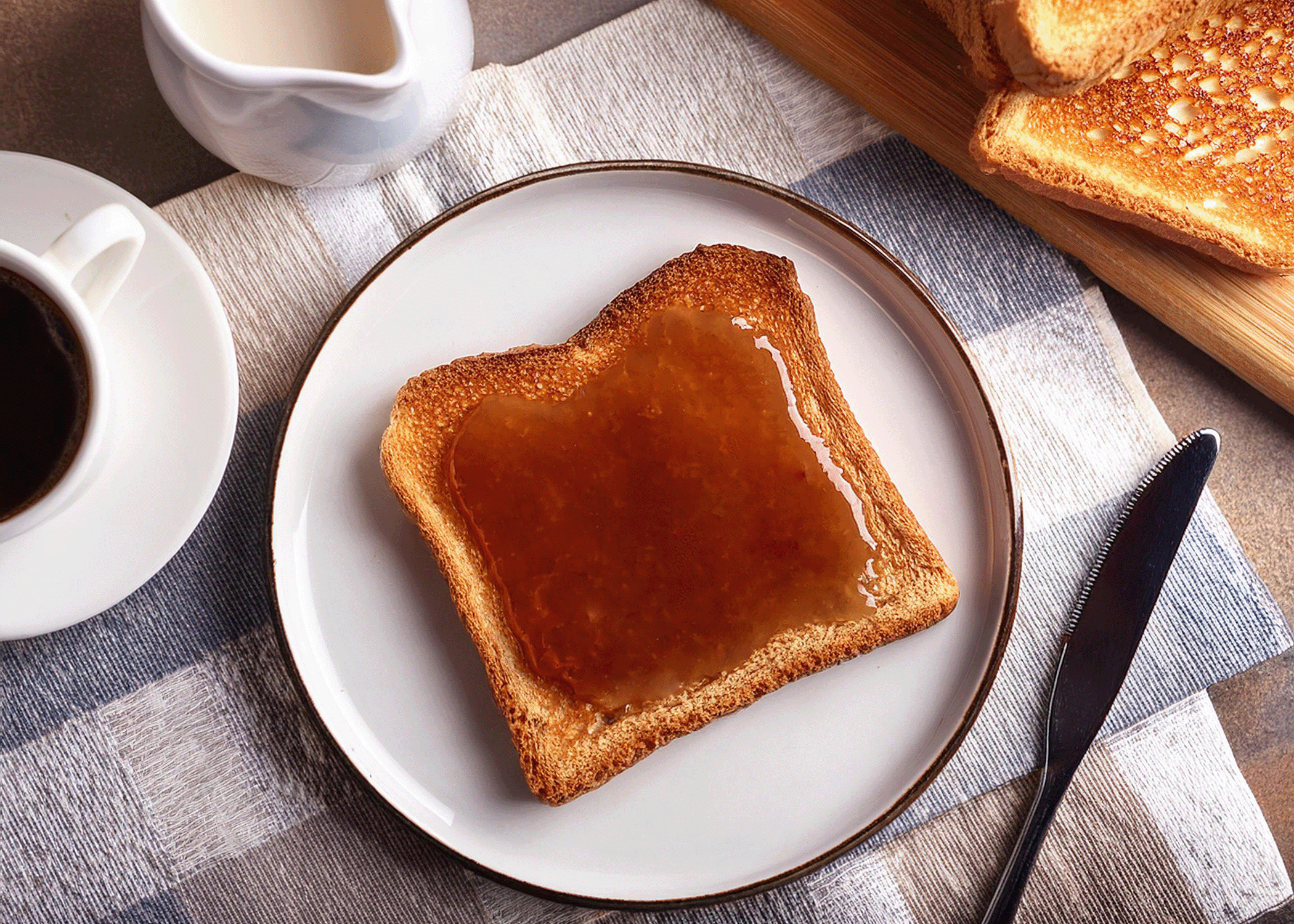 Toast with syrup on a plate next to a cup of coffee on a checkered tablecloth.