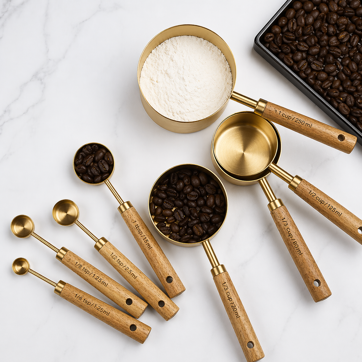 Set of gold measuring spoons with wooden handles on a marble surface with coffee beans and flour.