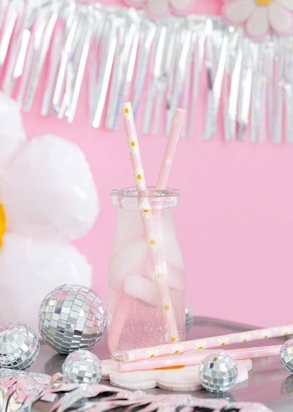 Glass with pink liquid and straws on a table with decorative items against a pink background