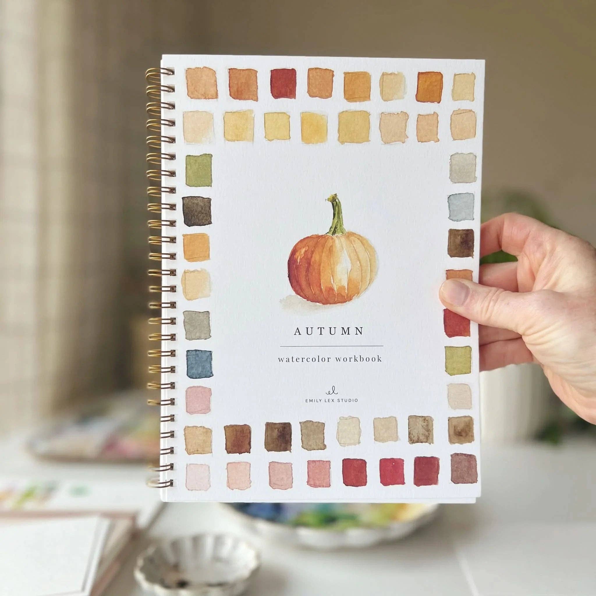 Notebook with autumn-themed cover featuring a pumpkin and color swatches, held by a hand.