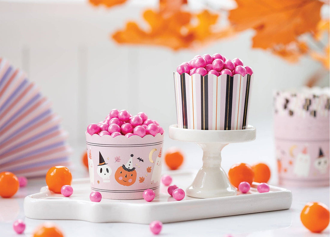 Two decorative treat cups filled with pink gummy candies, styled on a white tray with orange slices and autumn leaves in the background.
