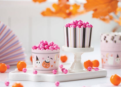 Two decorative treat cups filled with pink gummy candies, styled on a white tray with orange slices and autumn leaves in the background.