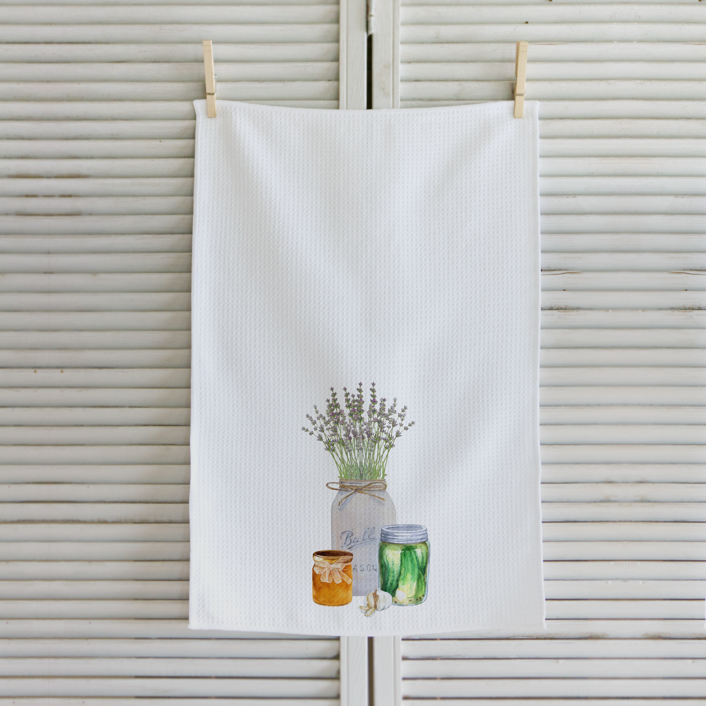 White tea towel with a design of jars and plants hanging on a wooden rack.
