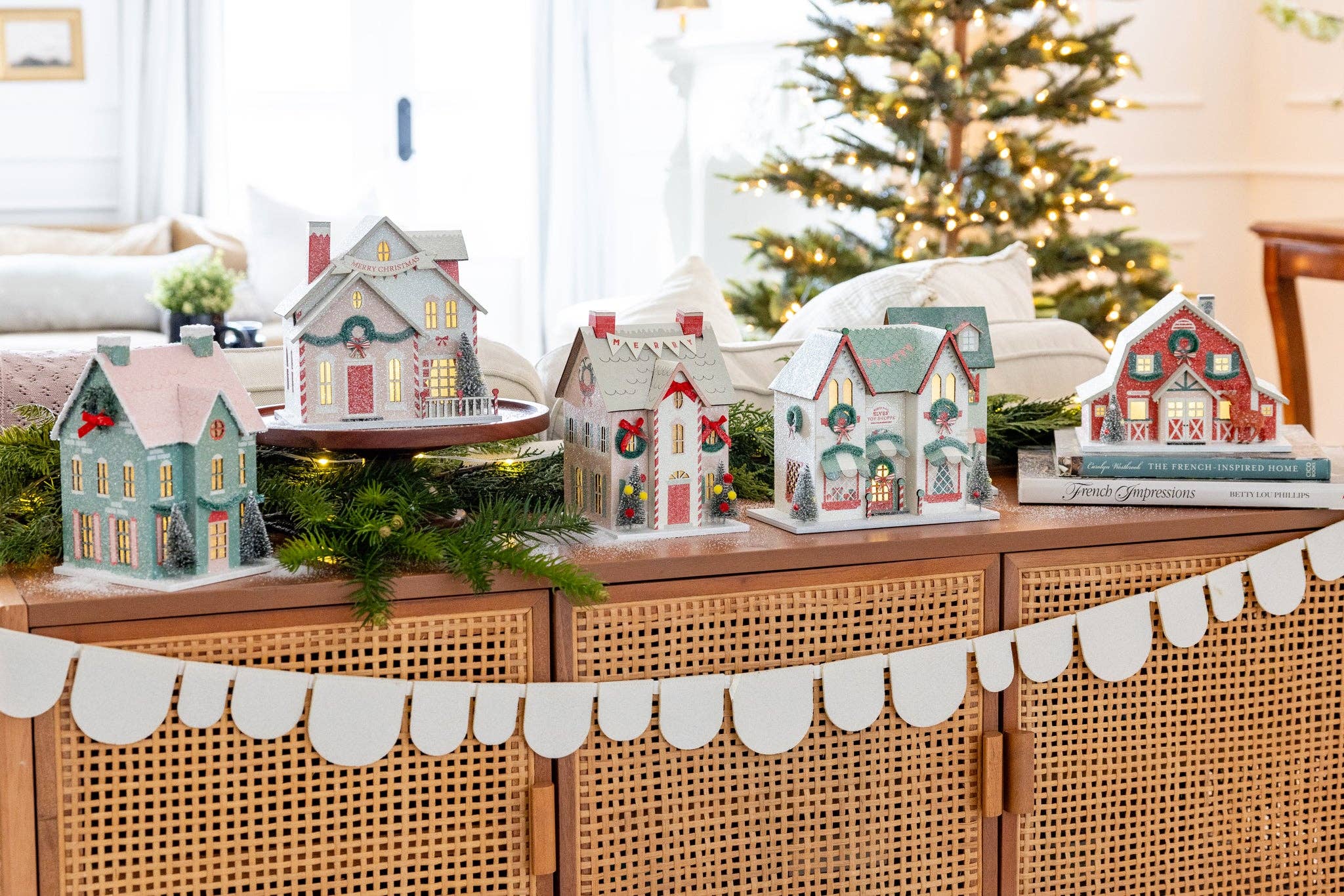 Decorative Christmas village houses on a console table with a Christmas tree in the background.