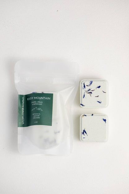 Two shower steamers with floral design on a white background, one still in packaging.