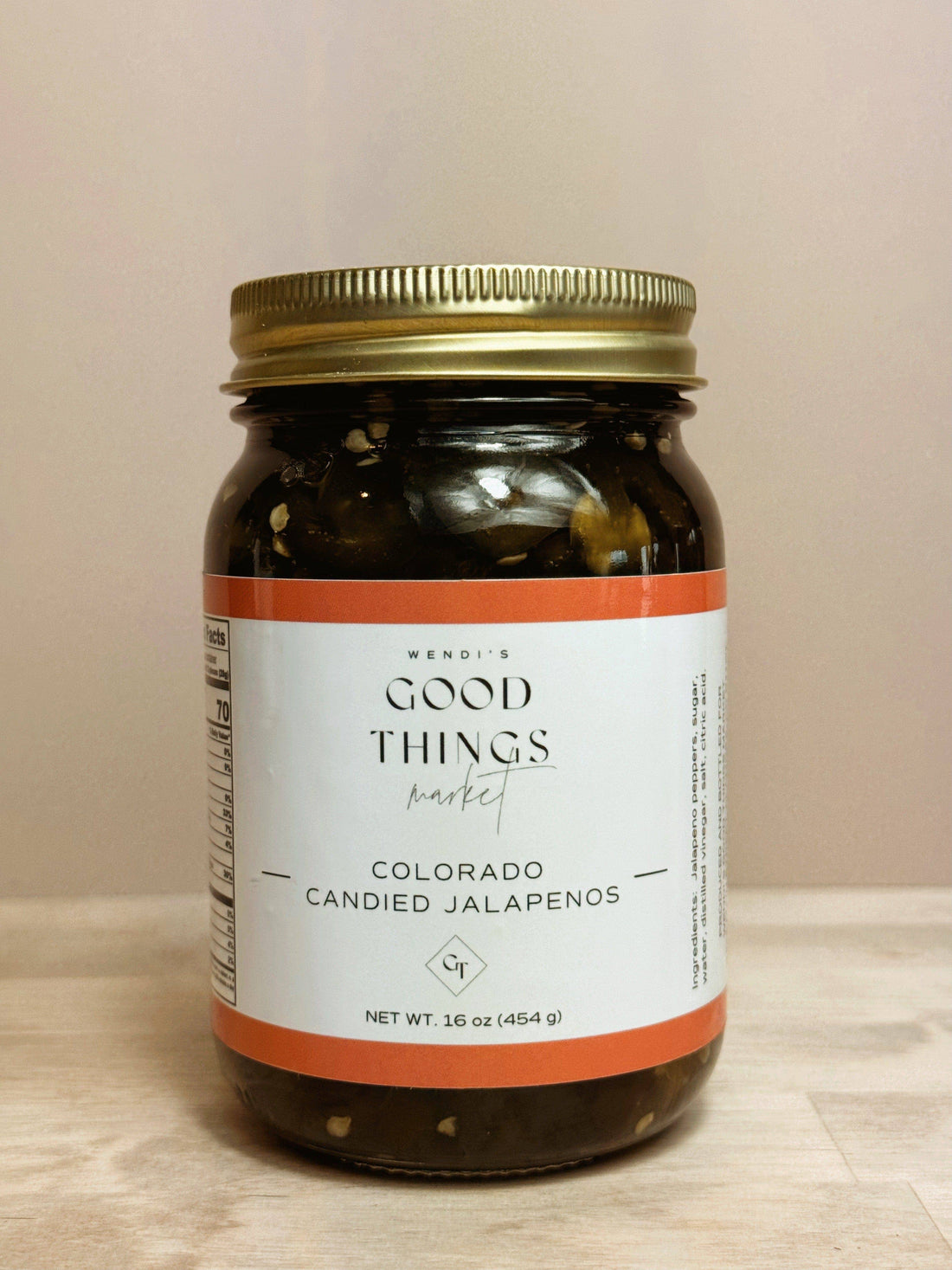 Jar of Colorado Candied Jalapenos with a gold lid on a wooden surface.