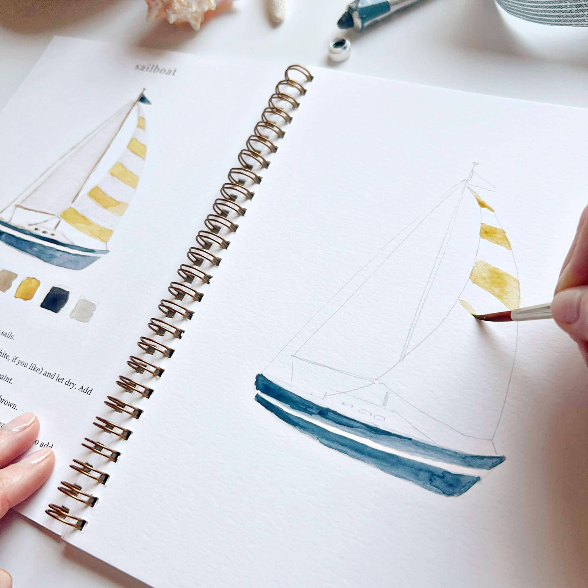 Person painting a sailboat illustration on a white surface with a paintbrush.