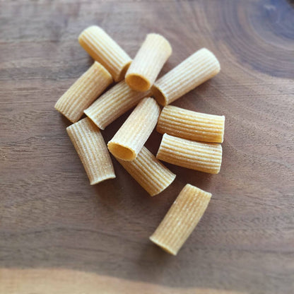 Several pieces of uncooked rigatoni pasta scattered on a wooden surface.