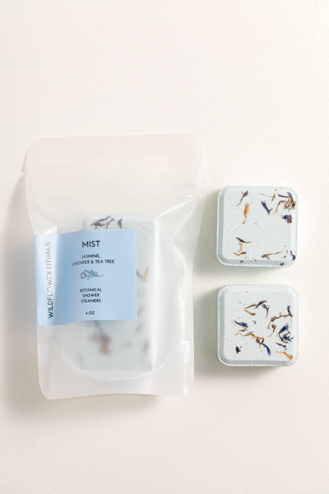 Three small shower steamer containers with labels on a light background