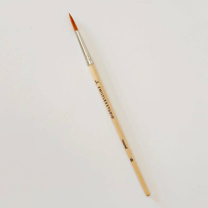 Paintbrush with wooden handle and gold ferrule on a light gray background
